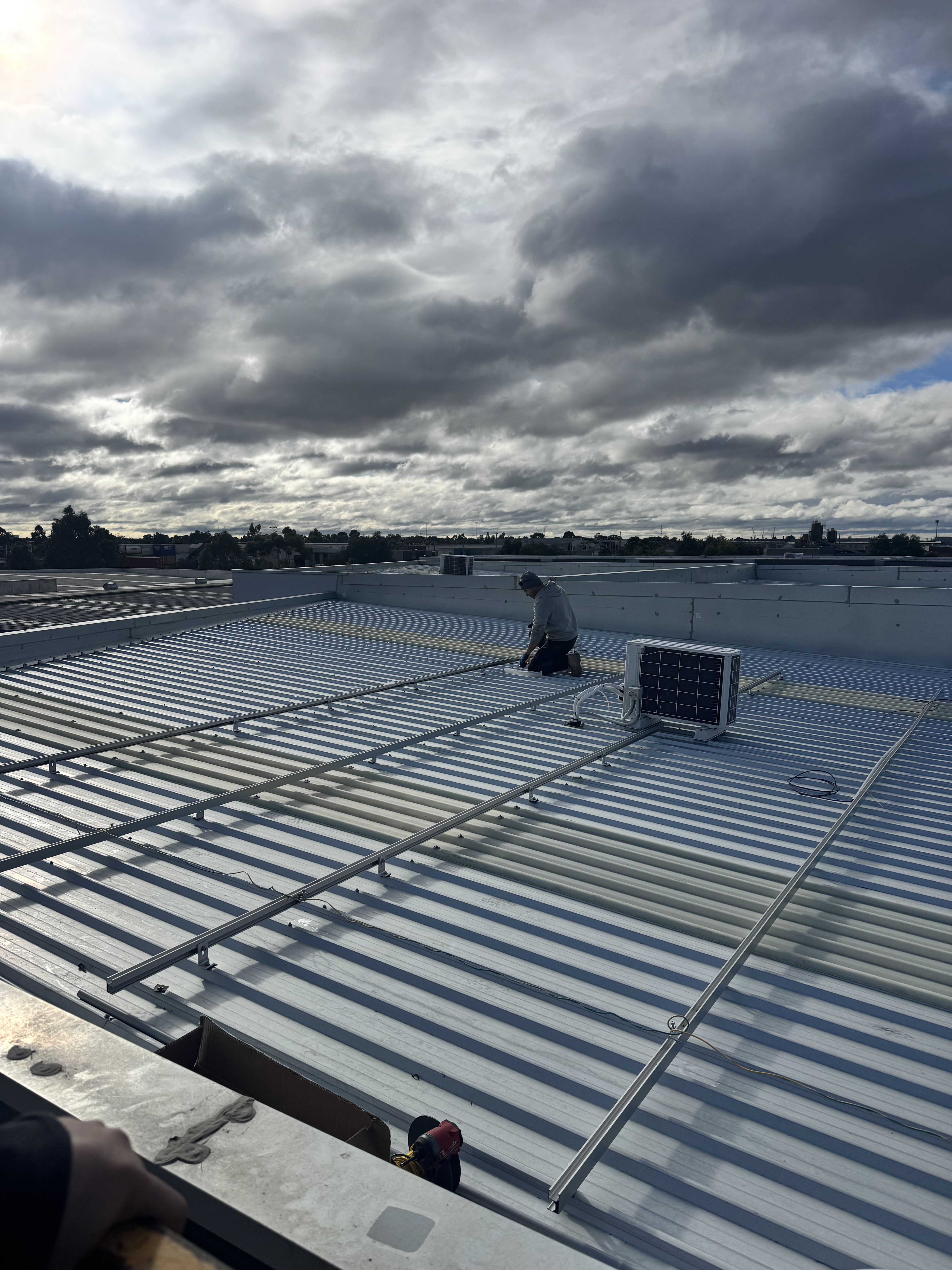 Installer fitting solar panel mounting rails on commercial warehouse roof